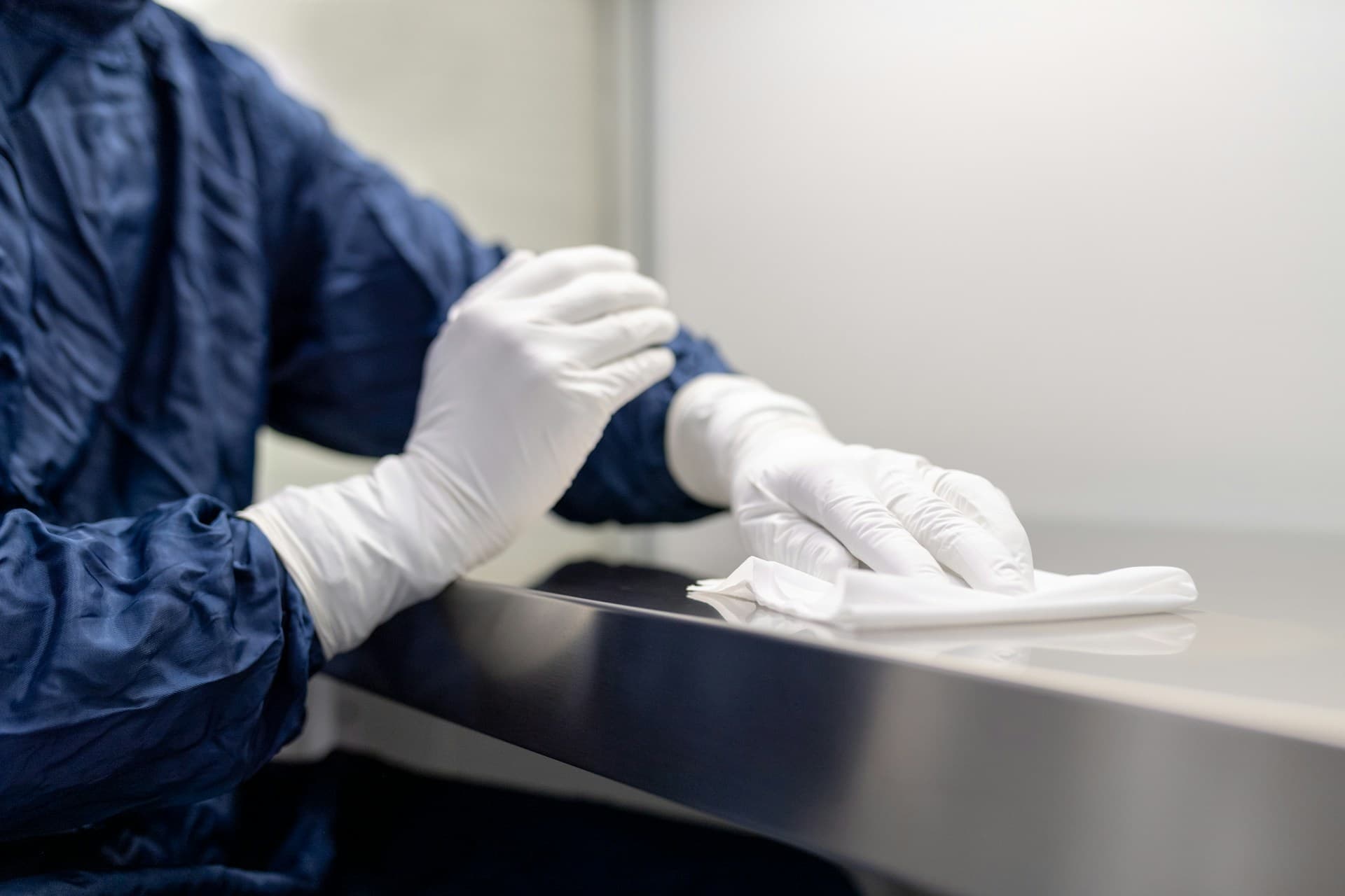 Gowned researcher wiping down a stainless steel surface in a controlled cleanroom environment